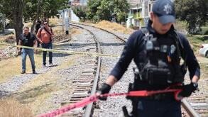 Policía sobre vías de tren sosteniendo una cinta roja de precaución.