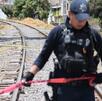 Policía sobre vías de tren sosteniendo una cinta roja de precaución.