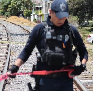 Policía sobre vías de tren sosteniendo una cinta roja de precaución.