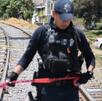 Policía sobre vías de tren sosteniendo una cinta roja de precaución.