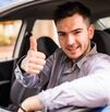 Un joven conductor sonríe mientras está al volante de su automóvil y hace una señal de aprobación con el pulgar.