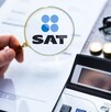 Mano sosteniendo una lupa con el logo del SAT delante de un documento con una calculadora, monedas y unos lentes a un lado