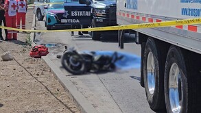 Motocicleta tumbada sobre el pavimento con una manta azul cubriendo a un hombre a un costado y paramédicos, patrullas y un camión alrededor
