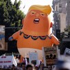 Inflable de Donald Trump caricaturizado como un bebé en medio de una multitud de manifestantes con letreros durante protestas en EU