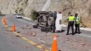Elementos de policía parados junto a una camioneta volcada en una carretera.