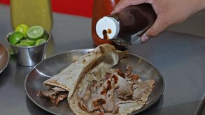Persona sirve salsa sobre un taco servido en una charola.
