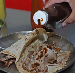 Persona sirve salsa sobre un taco servido en una charola.