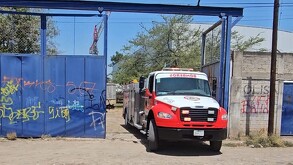 Camión de Protección Civil y Bomberos de Tlaquepaque saliendo de predio con portón azul y una grúa detrás