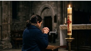 Persona rezando de espaldas en un templo con un cirio pascual encendido.