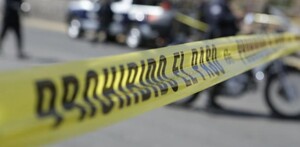 Cinta policiaca con la leyenda 'Prohibido el paso' acordonando un tramo carretero con patrullas y policías desenfocados en el fondo