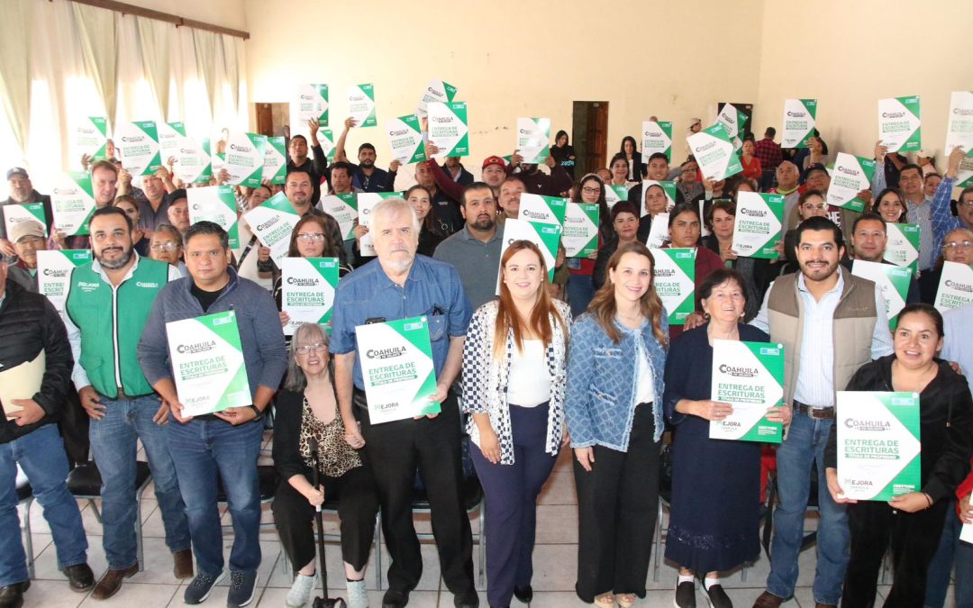 Grupo de personas sostiene documentos de escrituras en un evento oficial en Arteaga, relacionado con la regularización de predios y cabañas.