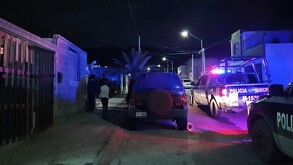 Se observa que es de noche, hay unas patrullas estacionadas y hay varias personas en la calle.