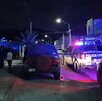Se observa que es de noche, hay unas patrullas estacionadas y hay varias personas en la calle.