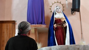 Mujer de espaldas rezando ante una figura religiosa en México.