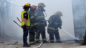 Se observa a unos bomberos sofocando un incendio, se ve humo.