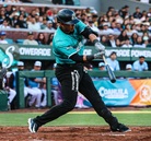 ugador de los Saraperos de Saltillo realiza un swing durante un partido, con uniforme verde y negro, en un estadio lleno de aficionados; al fondo se aprecia el