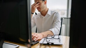 Un hombre se talla los ojos frente a la computadora de su oficina. Está estresado y casado porque no hay días feriados en abril.