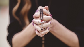 Mujer haciendo oración con un crucifijo en las manos y uñas color enero.