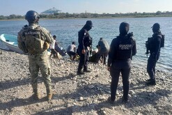 Tres oficiales de la Guardia Civil y un militar de la Marina observando a un grupo de hombres arrastrando una red a la orilla de un río con una lancha a un lado