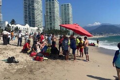 Paramédicos, elementos de Protección Civil de Puerto Vallarta y turistas rodeando a una persona en medio de la playa