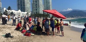 Paramédicos, elementos de Protección Civil de Puerto Vallarta y turistas rodeando a una persona en medio de la playa
