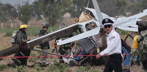 Policía camina junto a bomberos que realizan labores de rescate en una avioneta estrellada en Puebla.