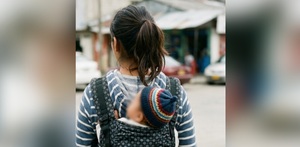una adolescente cargando a un bebé en su espalda