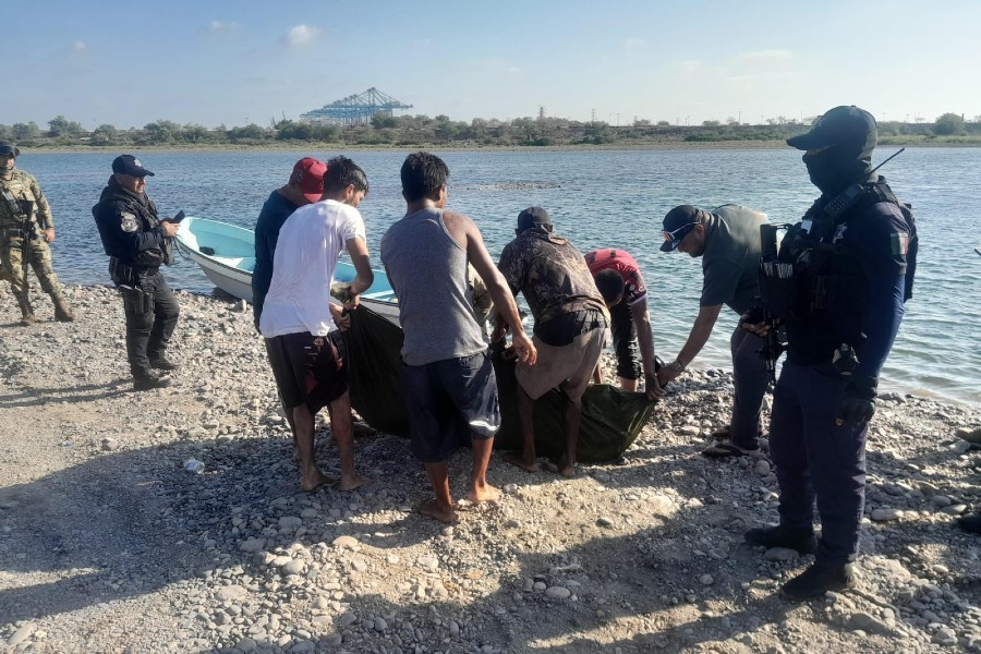 Grupo de hombres junto a oficiales de la Guardia Civil y militares de la Marina arrastrando una bolsa a la orilla de un río