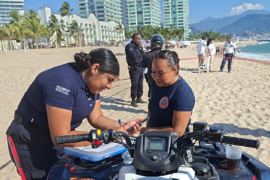Elementos de Protección Civil de Puerto Vallarta apoyadas en un cuatrimoto con policías detrás en medio de una playa
