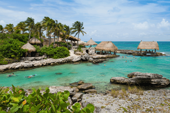Vista de una playa en Tamaulipas con agua de tonos azulados, palapas cercanas a la orilla, vegetación y visitantes disfrutando del entorno costero en un ambient