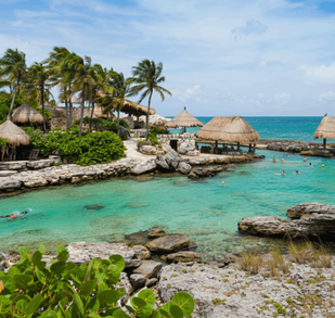 Vista de una playa en Tamaulipas con agua de tonos azulados, palapas cercanas a la orilla, vegetación y visitantes disfrutando del entorno costero en un ambient