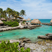 Vista de una playa en Tamaulipas con agua de tonos azulados, palapas cercanas a la orilla, vegetación y visitantes disfrutando del entorno costero en un ambient