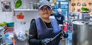 Mujer dentro de la cocina de un comercio en Jalisco sosteniendo unos cuchillos con ollas al frente y personas en el fondo