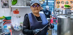 Mujer dentro de la cocina de un comercio en Jalisco sosteniendo unos cuchillos con ollas al frente y personas en el fondo