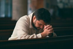 Hombre con la cabeza hacia abajo y las manos entrelazadas mientras ora en las bancas de una iglesia