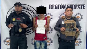 Se observa a tres hombres parados, el de enmedio viste una playera roja con pantalón de mezclilla y crocs color beige.