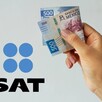 Una mano sosteniendo un billete doblado de 500 pesos mexicanos con un logo del SAT a un lado