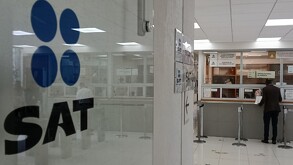 Puerta de oficinas del SAT con una apersona realizando un trámite al interior.