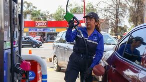 Mujer trabajadora de una gasolinera despacha el combustible a un vehículo.