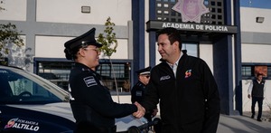 Javier Díaz saluda a una oficial de policía frente a la Academia de Policía de Saltillo, mientras una patrulla municipal y otros elementos se observan en el fon