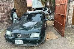Auto Volkswagen color negro saliendo de una vivienda con un camión detrás y militares alrededor