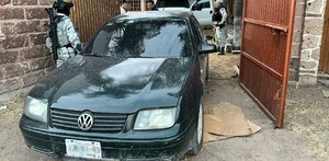 Auto Volkswagen color negro saliendo de una vivienda con un camión detrás y militares alrededor