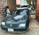 Auto Volkswagen color negro saliendo de una vivienda con un camión detrás y militares alrededor