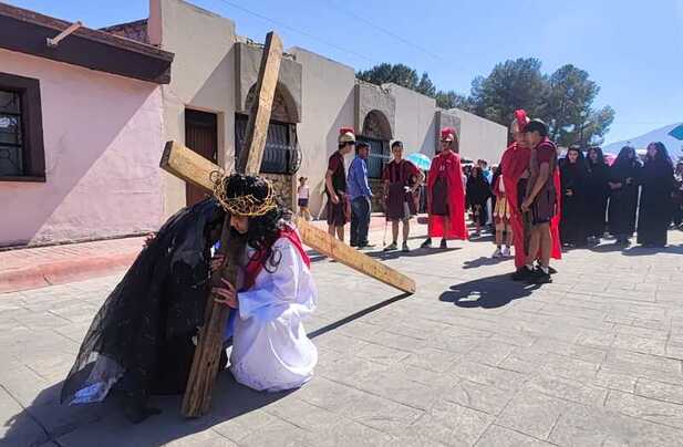 Joven representa a Jesús cargando la cruz en viacrucis viviente en Arteaga, seguido por soldados romanos y asistentes durante el recorrido.