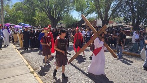 Imagen con efecto visual fragmentado de un recorrido al aire libre bajo árboles, donde se aprecia una escena relacionada con el viacrucis en Arteaga durante Sem