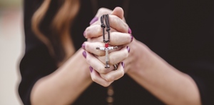 Mujer haciendo oración con un crucifijo en las manos y uñas color enero.