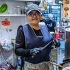 Mujer dentro de la cocina de un comercio en Jalisco sosteniendo unos cuchillos con ollas al frente y personas en el fondo