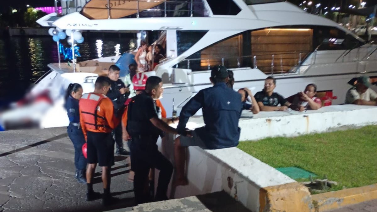 Grupo de personas, salvavidas y policías de Puerto Vallarta reunidos a bordo y alrededor de un yate a la orilla de un puerto en Vallarta