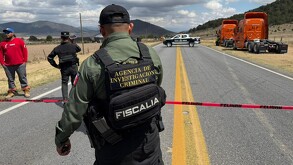 Se observa un policía, una cinta roja de precaución y un accidente al fondo.