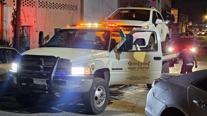 Imagen nocturna donde se observa una camioneta blanca remolcada por una grúa, con iluminación de patrullas y elementos alrededor